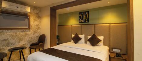A modern hotel room with a large bed, a seating area with a chair, a small table, and a wall-mounted air conditioning unit.