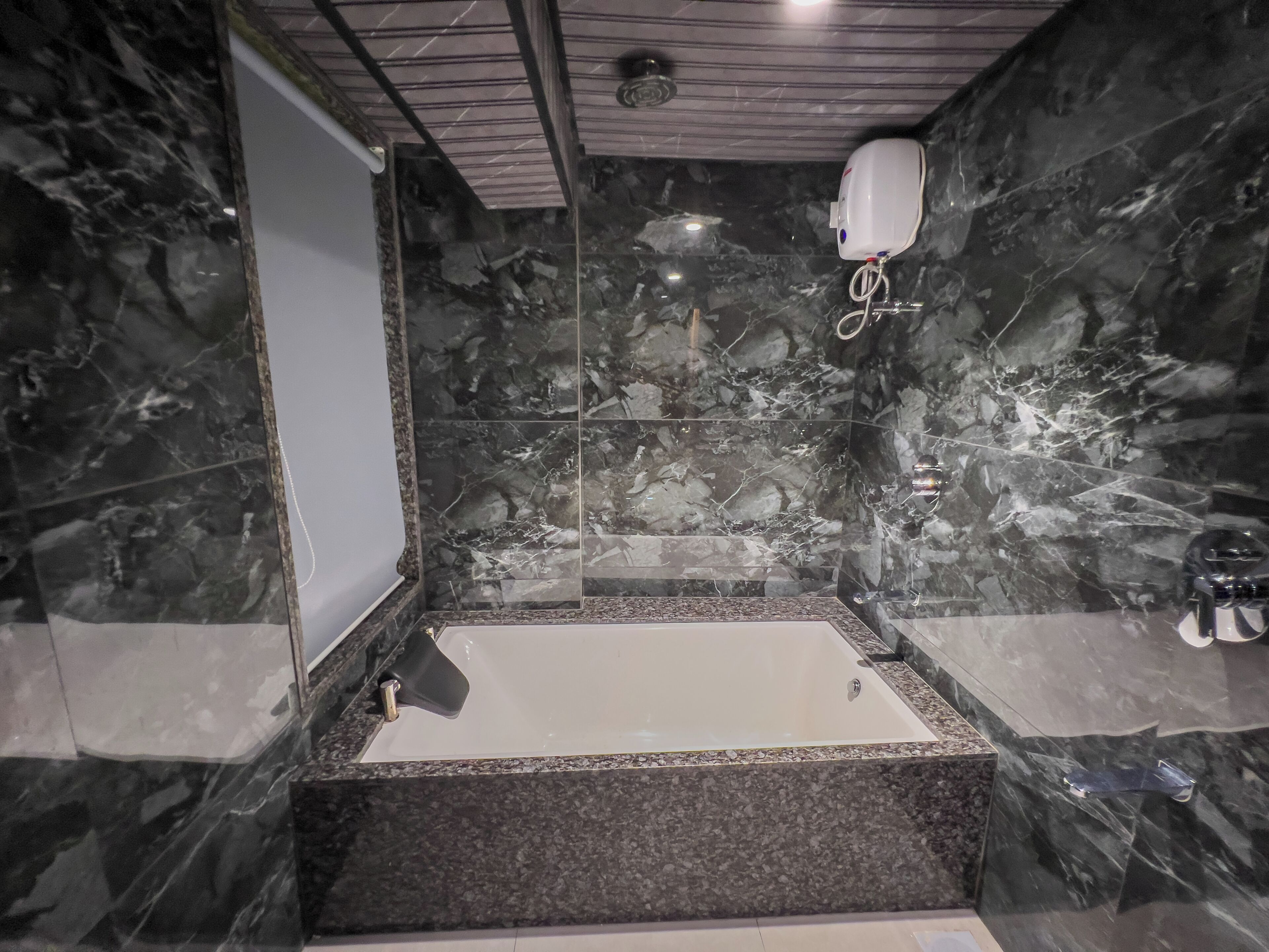 A modern bathroom with a marble shower wall, a bathtub, and a handheld showerhead.