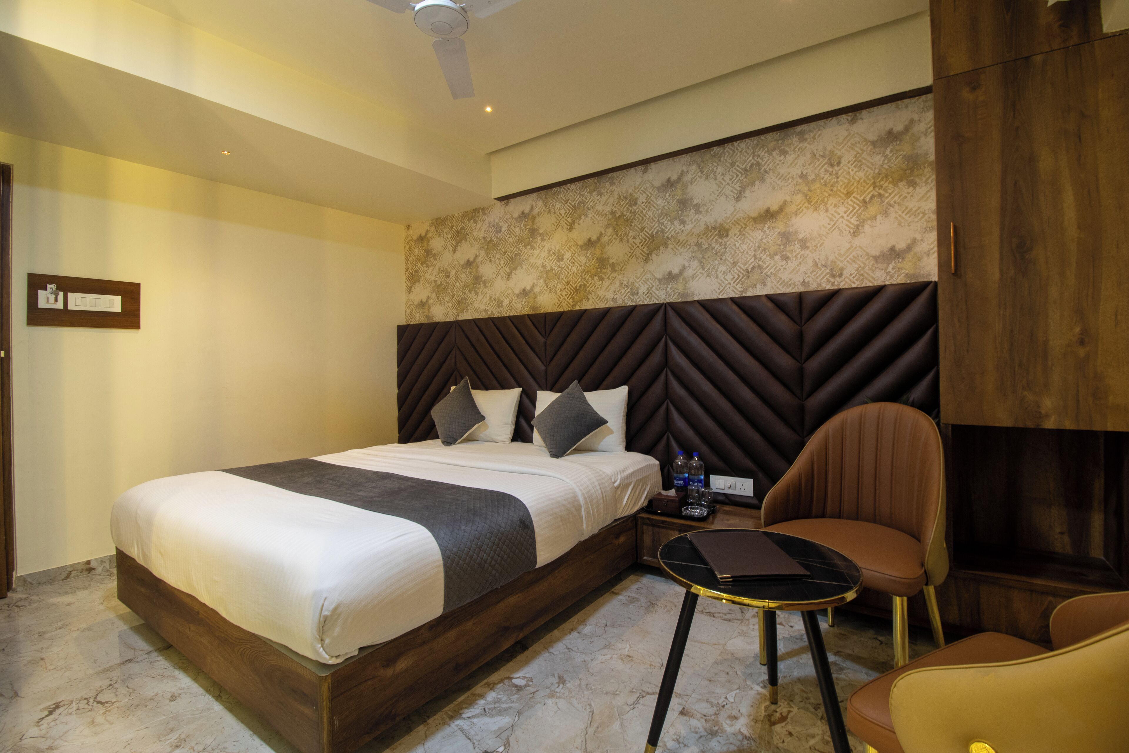 A hotel room with a large bed, a wooden headboard, a small table, and two chairs.