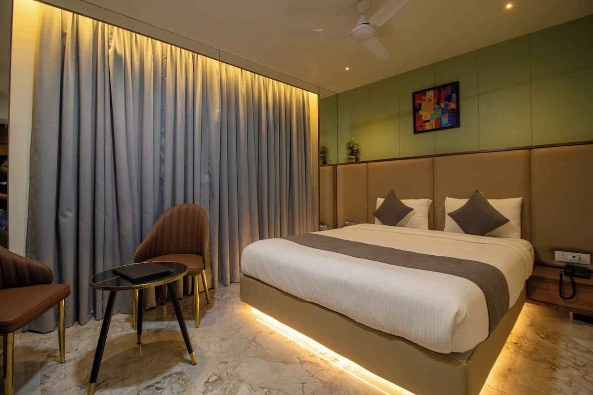 A hotel room with a large bed, a small table, two chairs, a ceiling fan, and a painting on the wall.