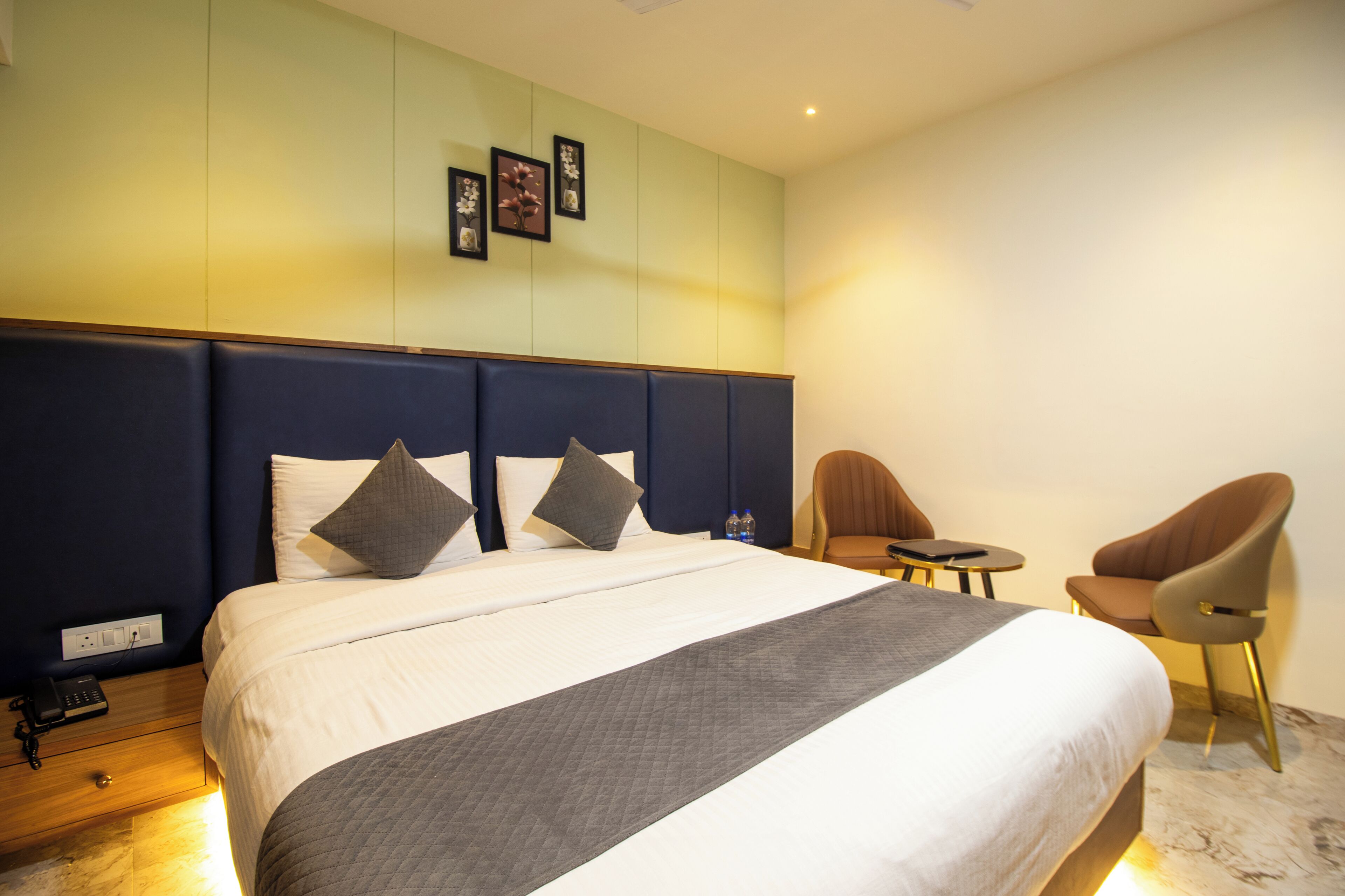 Una habitación de hotel con una cama grande, dos sillas, una mesita pequeña y un teléfono en la pared.