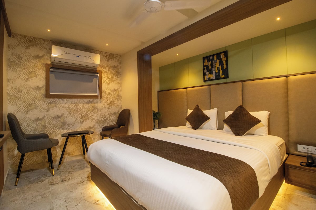 A modern hotel room with a large bed, two chairs, a small table, and an air conditioning unit mounted on the wall.