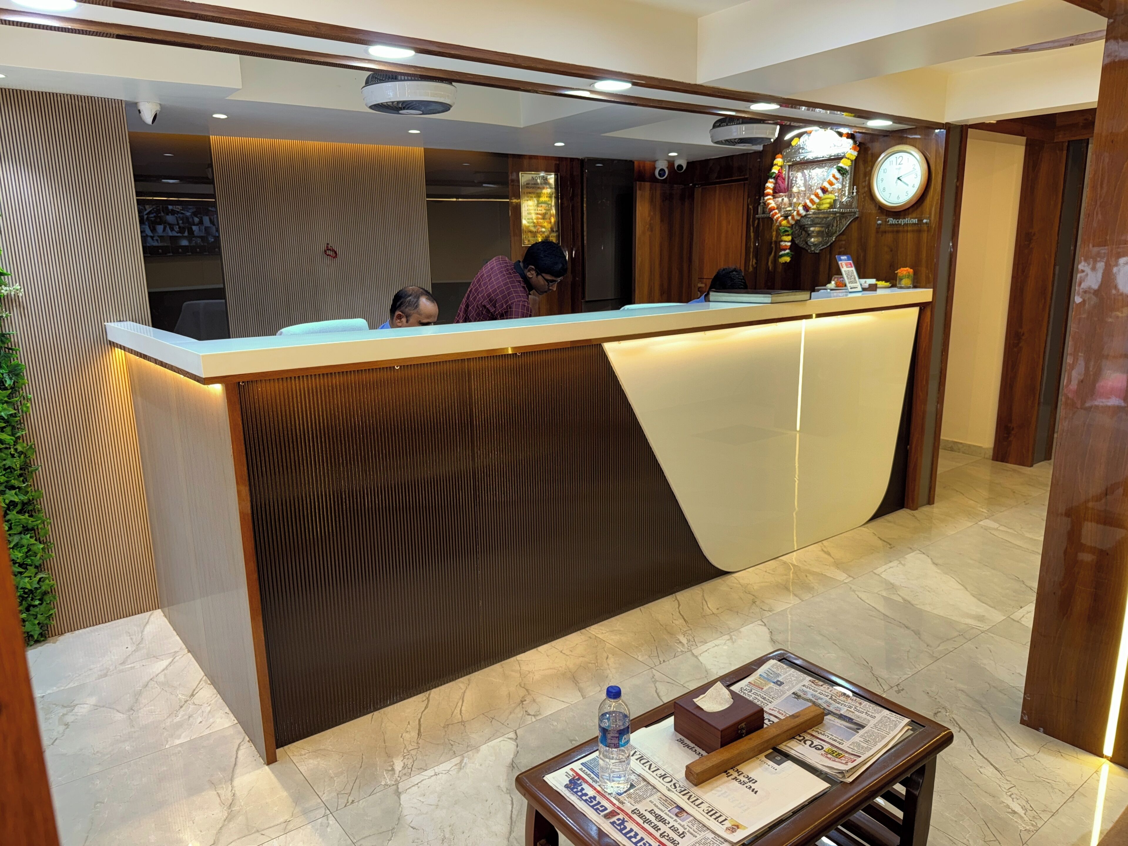 A reception desk with a wooden finish and a modern design, a clock, and a reception area with a tiled floor.