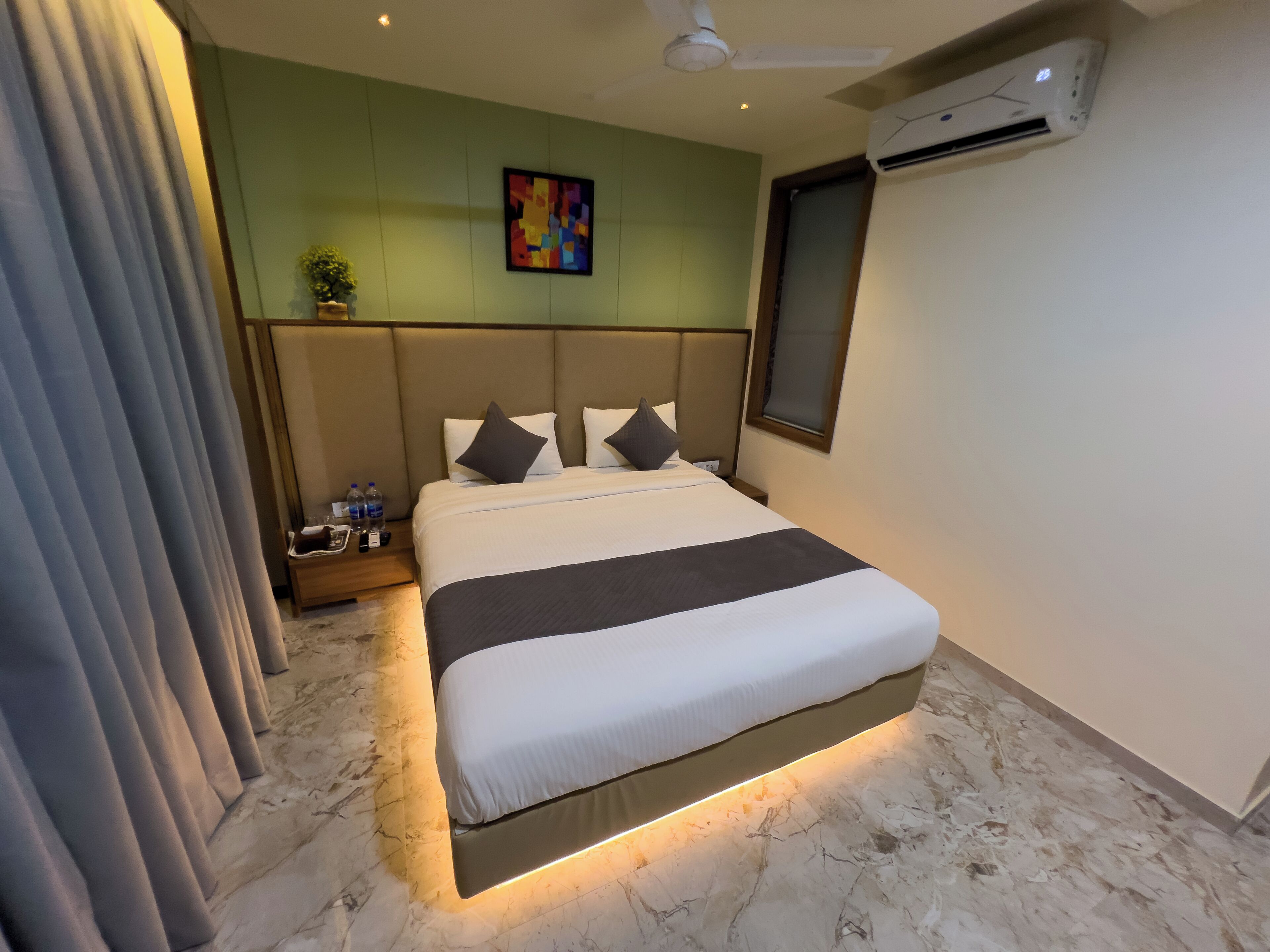 A hotel room with a bed, a nightstand, a potted plant, and an air conditioning unit.