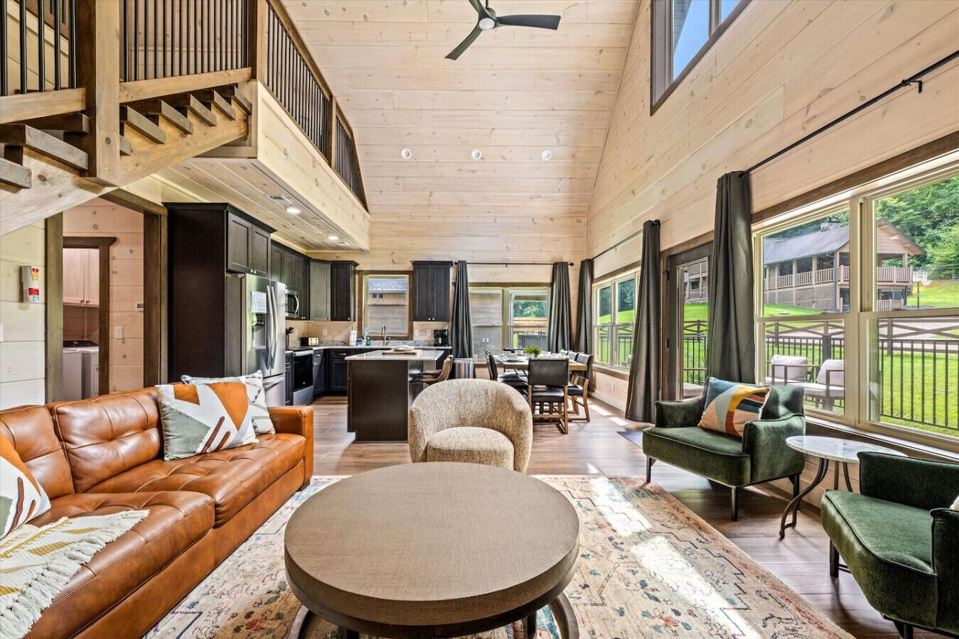 A spacious living area with a high ceiling, wooden beams, a central island, and large windows offering views of the outdoors.