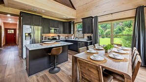 Une cuisine moderne avec des meubles de couleur sombre, un îlot central et un coin repas avec une table dressée pour quatre personnes.