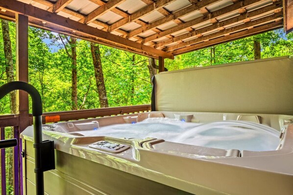 A hot tub in a covered outdoor area with a wooden ceiling and a view of lush green trees.