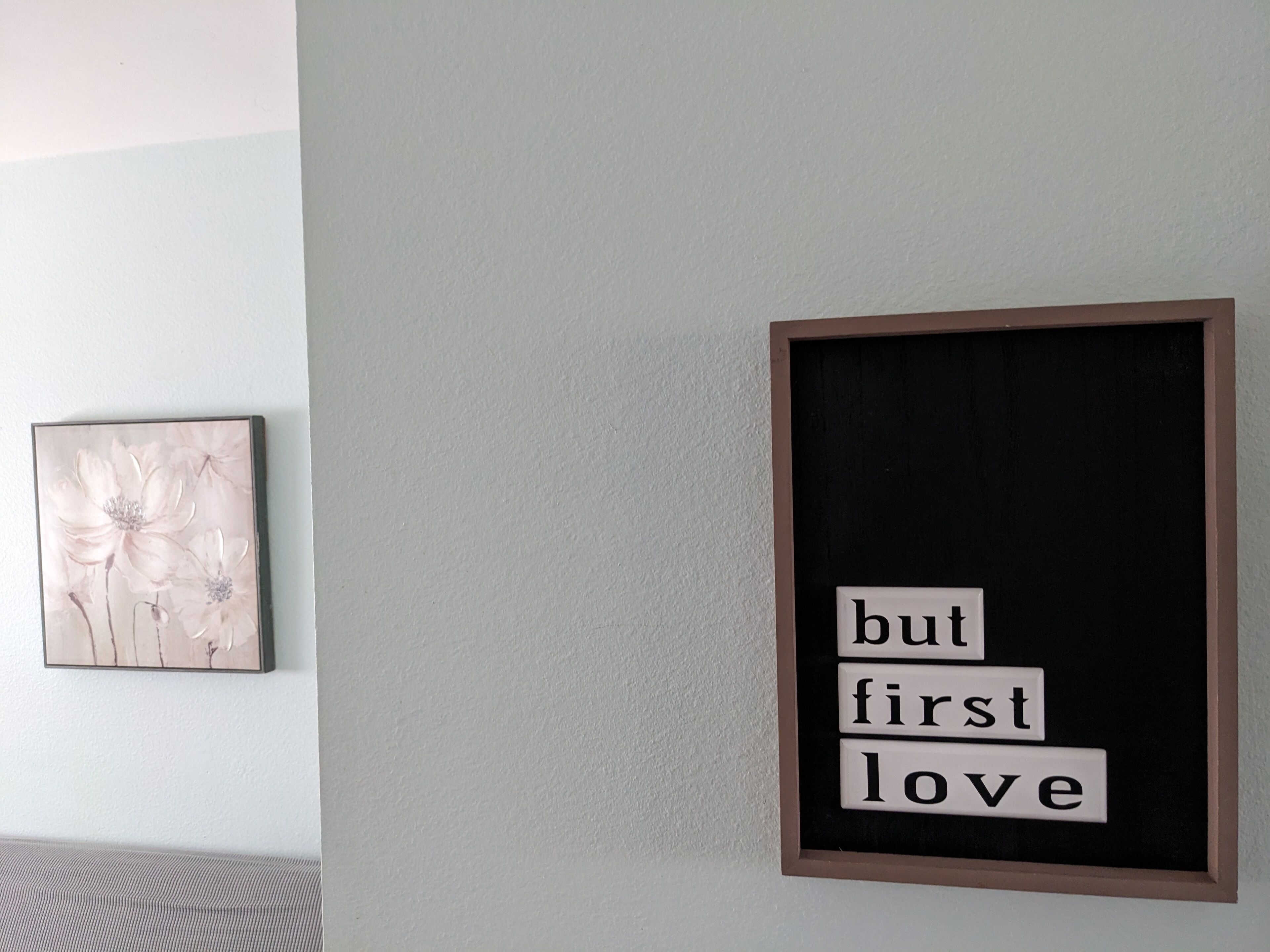 Ein gerahmtes Zitat an einer Wand, ein gerahmtes Blumenbild und eine strukturierte Wand.