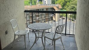 A balcony with a table and two chairs, a view of a green landscape, and a building in the background. - New! *Walk to Gatlinburg!* 2BR w/Balcony*Comm Pool (Gatlinburg)