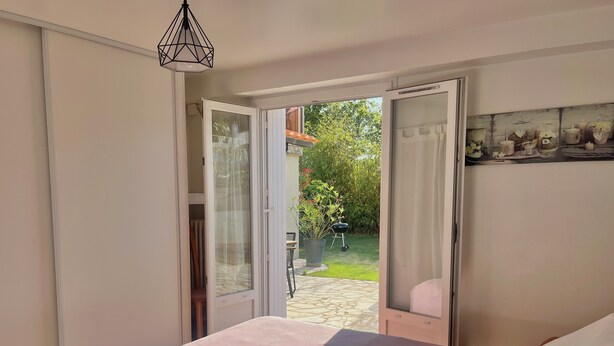 A bedroom with a bed, a window, and an open door leading to a garden.