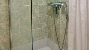 A glass-enclosed shower with a handheld showerhead and a wall-mounted faucet.