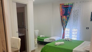 A hotel room with two single beds, a bathroom with a sink, and a view of the outside through a window with patterned curtains. - Corte Vena Palace (Bianco)