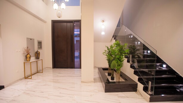 A modern interior with a marble floor, a staircase with glass railings, and a dark wooden door. - Luxury 5 Bedroom Villa Nad Al Sheba (Dubai)