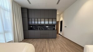 A modern hotel room with a built-in kitchen, wooden flooring, and a large window with sheer curtains. - Luxury 5 Bedroom Villa Nad Al Sheba (Dubai)