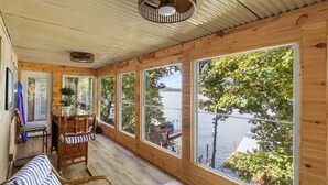 A wooden cabin with large windows overlooking a lake, a small table with chairs, and a ceiling fan. - Waterfront Home with Bunkhouse (Rocky Mount)