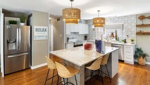 A modern kitchen with a central island, stainless steel appliances, wicker pendant lights, and a 'RELAX' sign. - Waterfront Home with Bunkhouse (Rocky Mount)