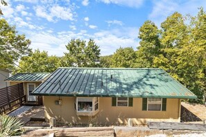 A single-story house with a green metal roof, a small front porch, and a visible window.