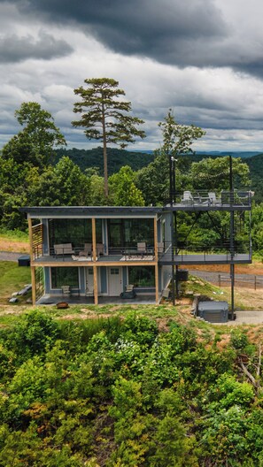 A modern house with a glass facade, a deck, and a view of the surrounding forest.