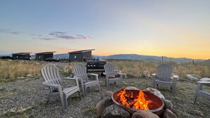 Ein Campingplatz mit Adirondack-Stühlen, einer Feuerstelle und einem Grill.