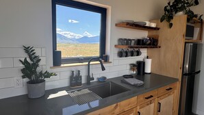 Eine moderne Küche mit Blick auf Berge, einem Spülbecken, Holzschränken und einem Edelstahlkühlschrank.