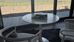 Ein Zimmer mit einem runden Tisch und zwei Stühlen, mit Blick auf eine Wüstenlandschaft durch große Fenster, und einige Bücher auf dem Tisch.