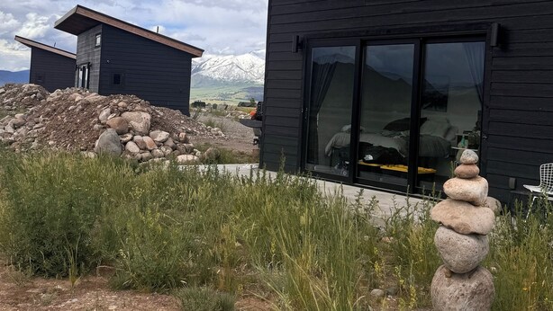 Eine moderne Holzhütte mit einer großen Glasschiebetür, eingebettet in eine natürliche Landschaft mit einer Steinhaufen im Vordergrund.