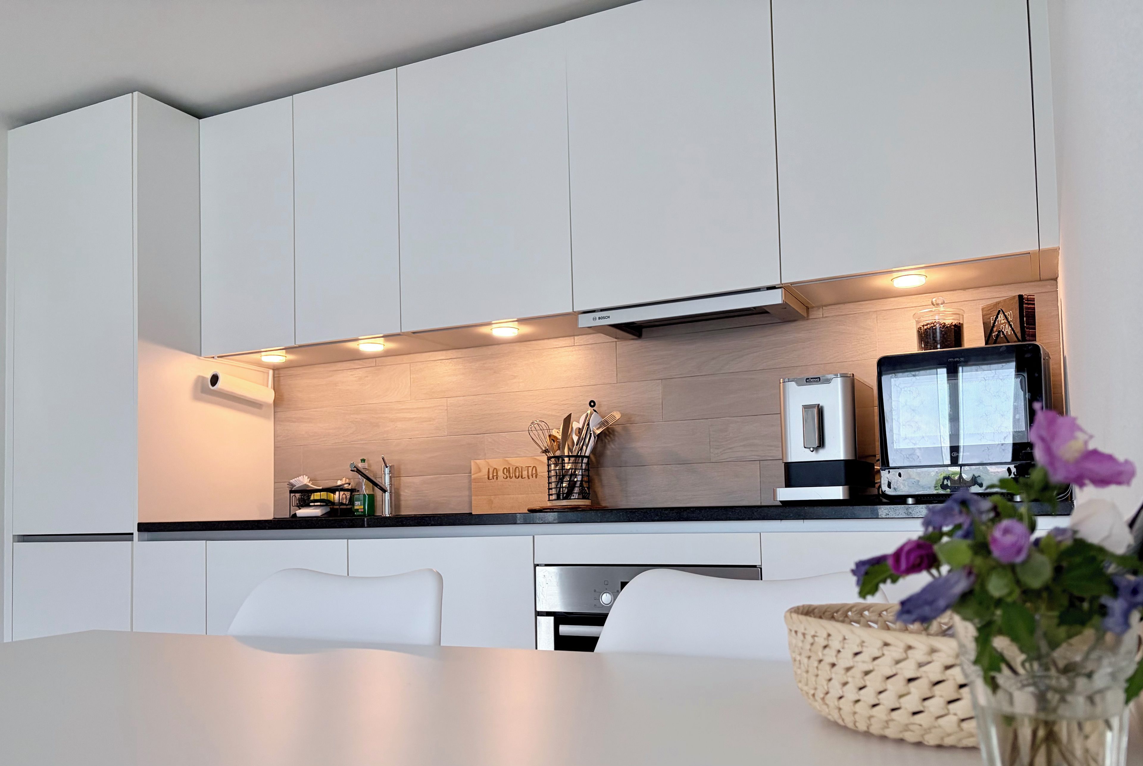 A modern kitchen with white cabinets, a black countertop, and a Bosch coffee machine.