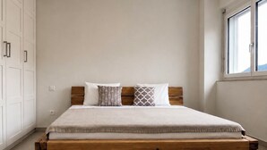 A bed with a wooden frame, a white mattress, and patterned pillows. There is a window on the right side. - Residenza La Svolta - Salt Pool & Private Garden (Bellinzona)