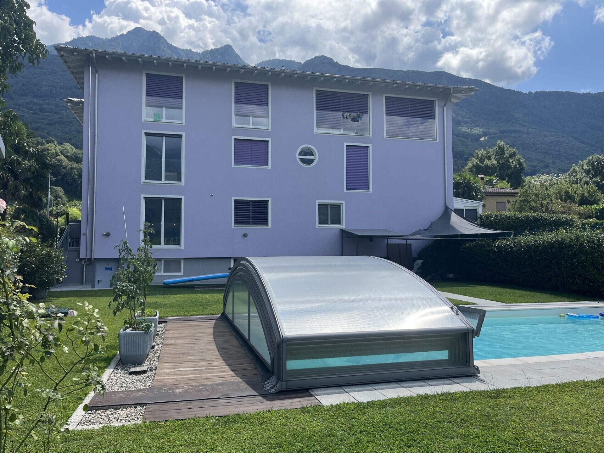 Una casa de dos pisos con piscina, rodeada de vegetación y montañas.