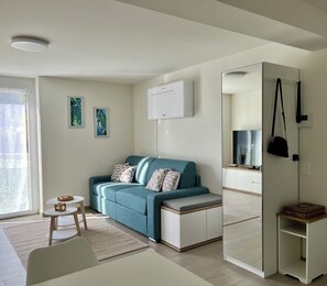 A modern living room with a sofa, a small table, a mirror, and a window.