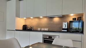 A modern kitchen with white cabinets, a glass-top dining table, a Bosch coffee machine, and a digital display. - Residenza La Svolta - Salt Pool & Private Garden (Bellinzona)