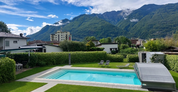 A swimming pool with lounge chairs, a small garden, and a mountain backdrop.