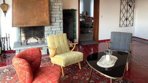 Un salon chaleureux avec une cheminée, deux fauteuils, une petite table et, au fond, un coin repas.
