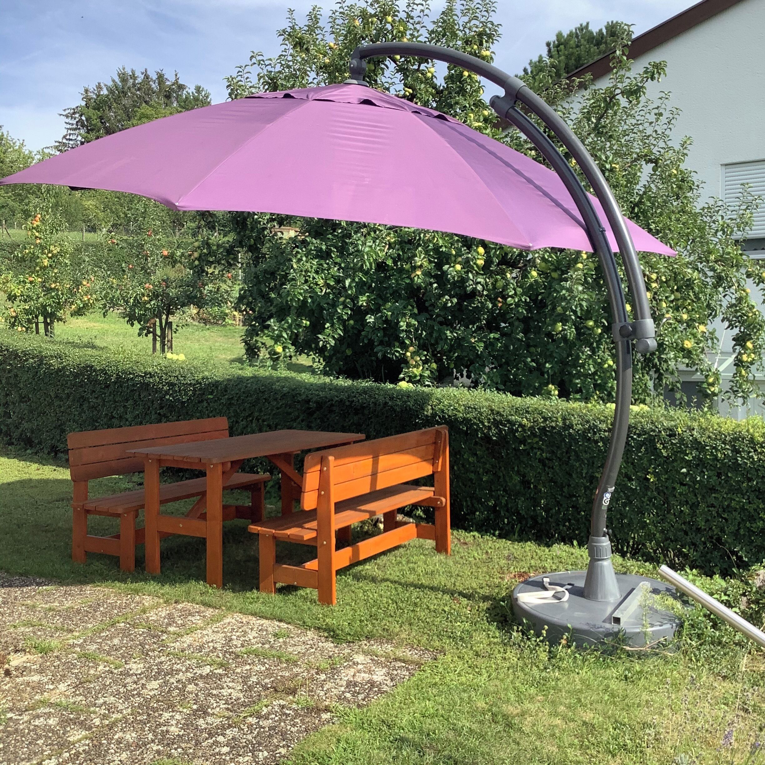 A wooden bench and a purple umbrella in a garden.
