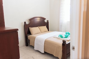 Una cama bien hecha con cabecera de madera, colcha color beige y manta blanca.