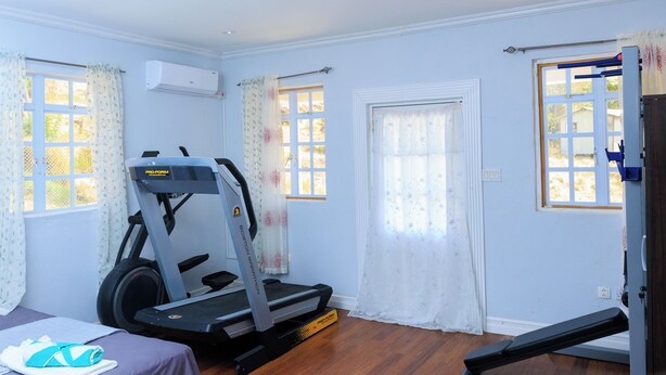 Ein Zimmer mit Laufband, Massagetisch und einem Fenster mit Vorhängen.
