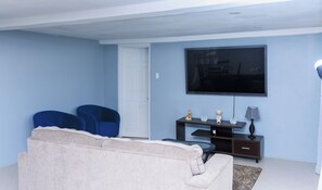 A living room with a beige sofa, two blue armchairs, a flat-screen TV mounted on the wall, a small table with decorative items, and a lamp. -    4-bedroom house in marvelous Choiseul with fitness room, AC (Delcer)