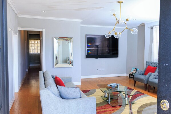 A modern living room with a grey sofa, a glass coffee table, and a mounted TV.
