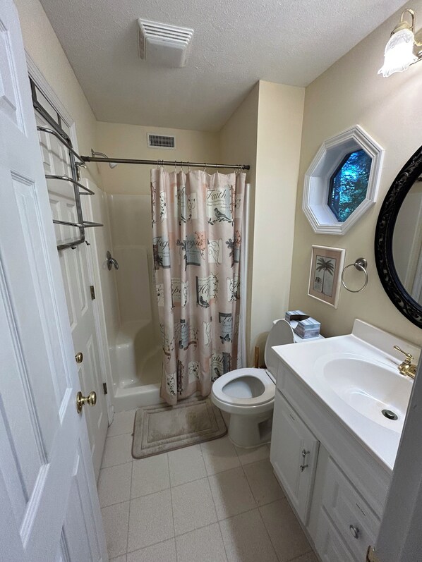 Un baño con cortina de ducha, inodoro, lavabo y ventana con vistas a árboles.