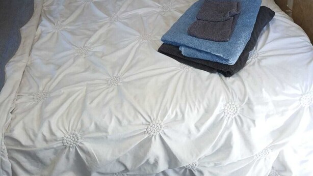 Een enkel bed met een witte gewatteerde sprei en een opgevouwen handdoek erop.