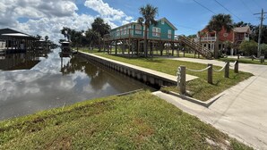 Una propiedad frente al agua con un canal, un muelle de madera y una casa elevada sobre pilotes.