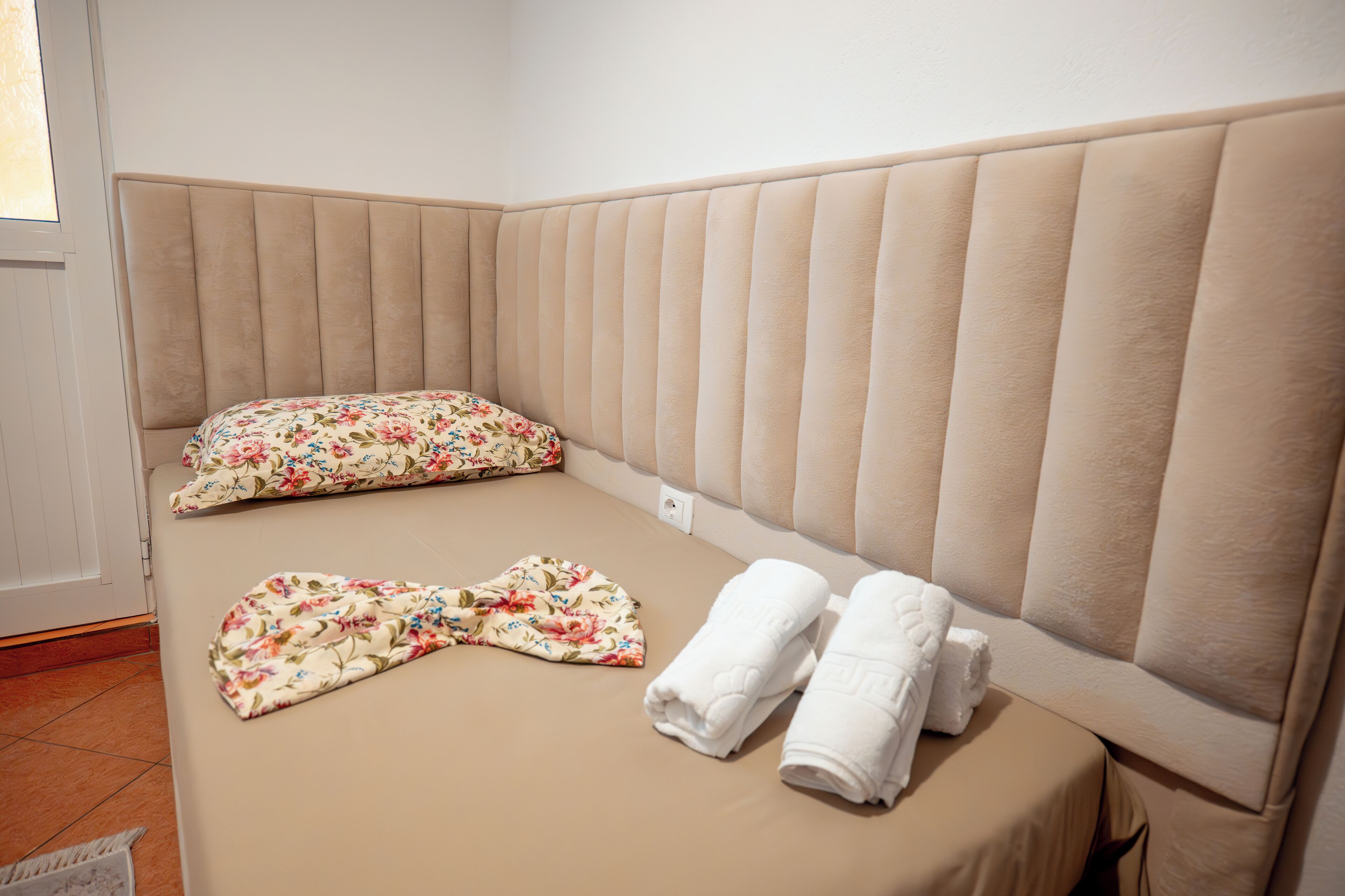Un lit bien fait, avec un oreiller à motifs floraux et deux serviettes soigneusement pliées.