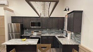 A modern kitchen with dark cabinets, stainless steel appliances, a marble countertop, and a dining area with wooden chairs.