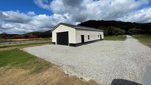 A single-story building with a large garage door, surrounded by gravel, with a clear sky and hills in the background.