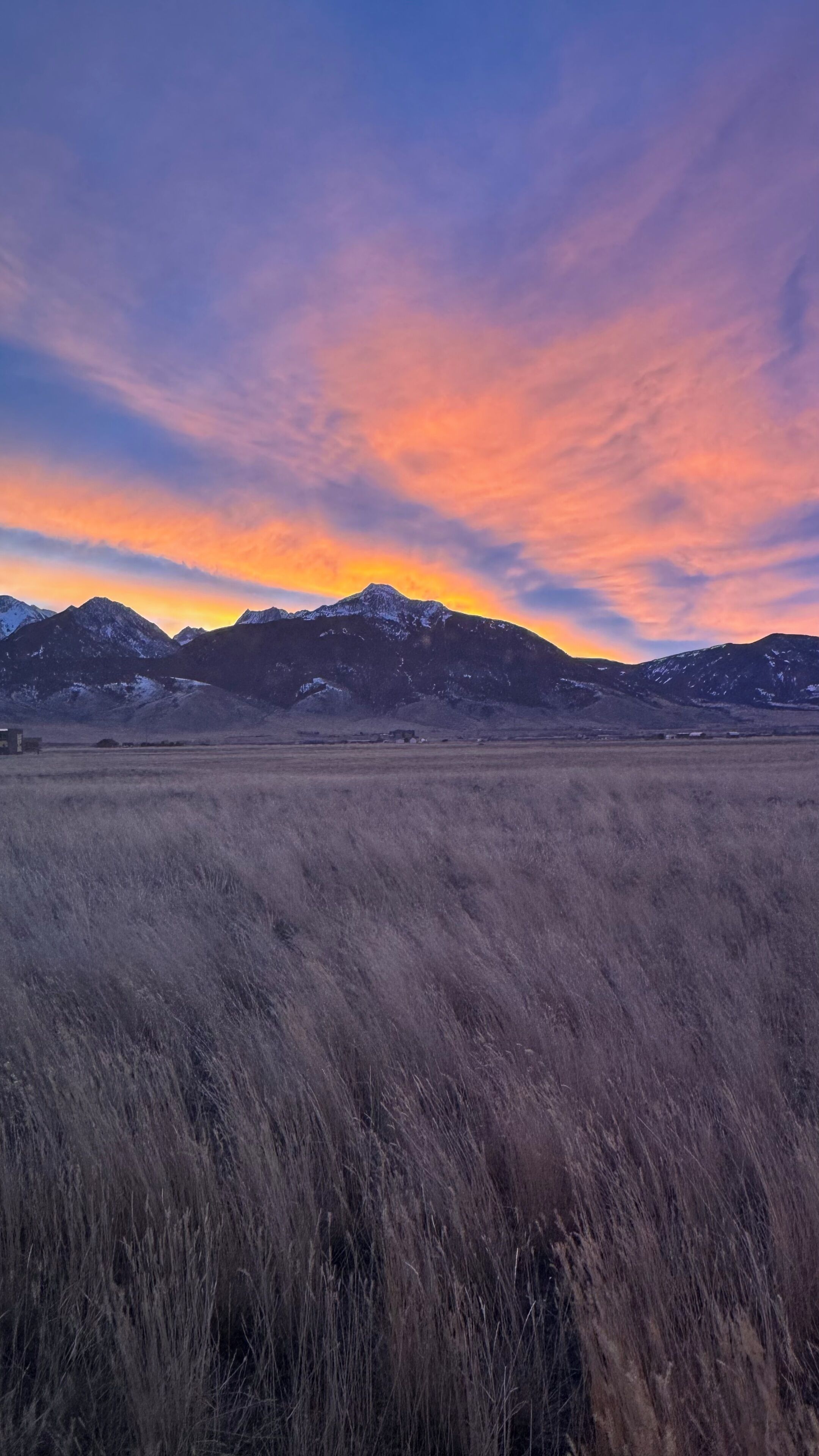 A mountainous landscape with a field in the foreground and a sunset in the background.