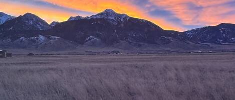 A mountainous landscape with a field in the foreground and a sunset in the background.