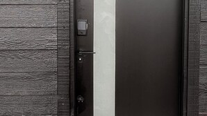 A dark wooden door with a vertical strip, a number '3' sign, and a small light fixture above it.