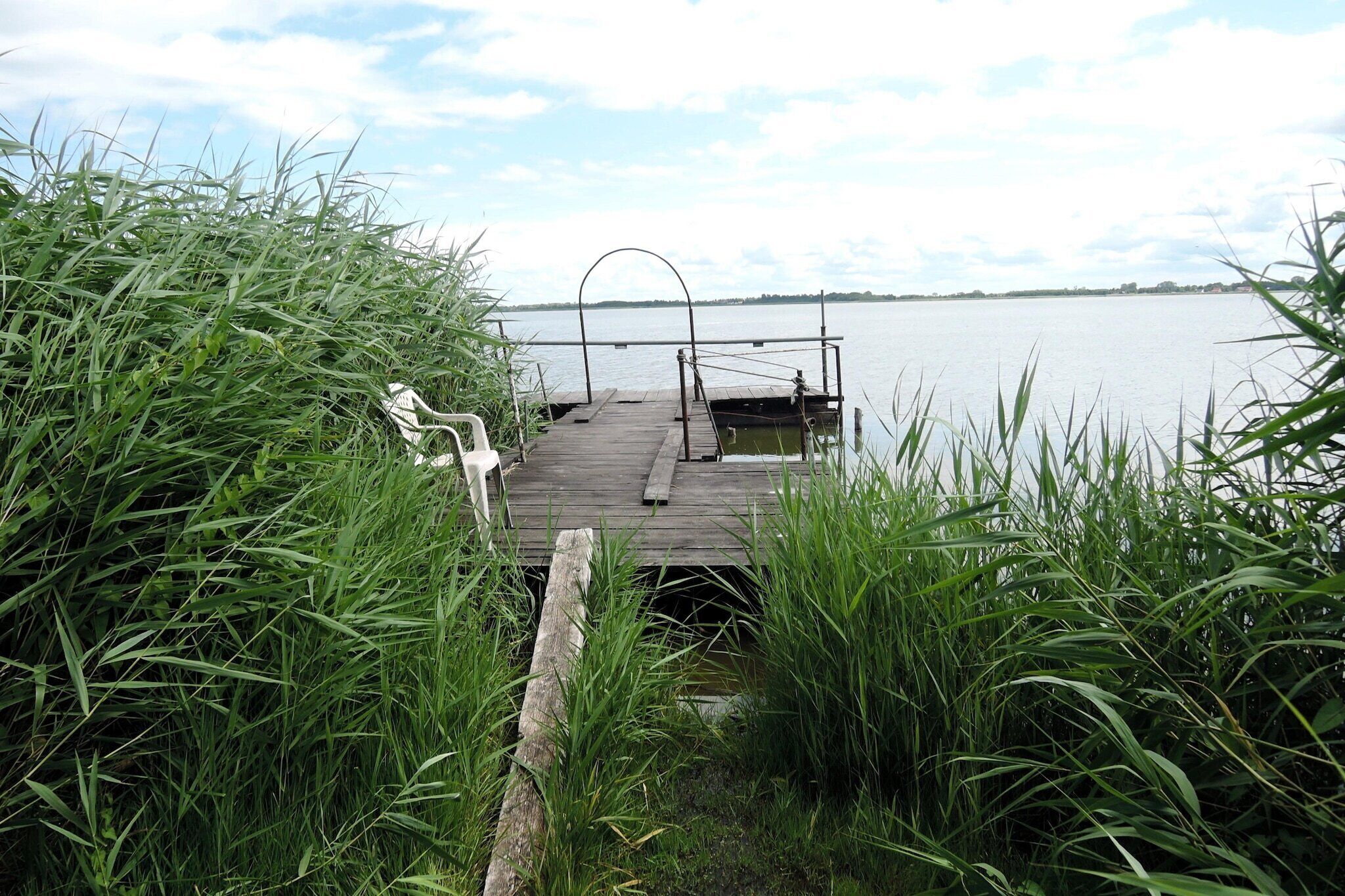 Une jetée en bois s’étendant sur un lac paisible, entourée de hautes herbes.