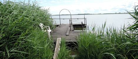 Une jetée en bois s’étendant sur un lac paisible, entourée de hautes herbes.