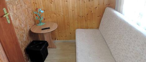 A small room with a wooden wall, a round wooden table with a plant, a black storage box, and a beige sofa.